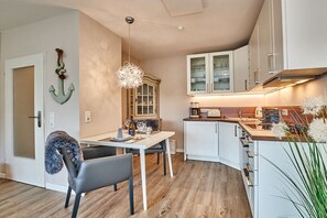 A modern kitchen with white cabinets, a dining area with a table and chairs, and a decorative anchor on the wall. - Tastefully furnished 2-room holiday apartment "Happy Dreams" (Westerland)