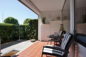 A patio with a table and chairs, a potted plant, and a glass door leading to a garden. - Tastefully furnished 2-room holiday apartment "Happy Dreams" (Westerland)