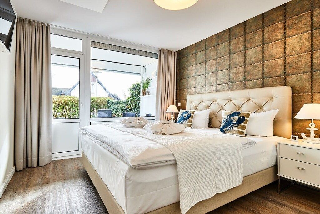 A modern bedroom with a large bed, a view through a sliding door, and a textured wall.