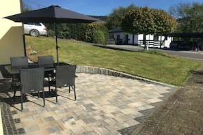 Un espace extérieur aménagé en terrasse, avec une table et des chaises, un parasol noir et un sol recouvert de carreaux de pierre.