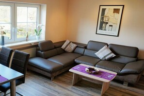 Ein modernes Wohnzimmer mit einer Eckcouch, einem kleinen Tisch und einem Fenster mit Pflanzen.