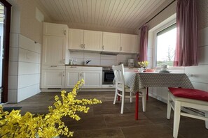 Et køkken med hvide skabe, et spisebord med dug og et vindue med gardiner.