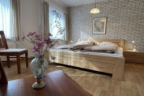 A bedroom with a wooden bed, a vase with flowers, a wooden table, and a brick wall. - "Mullewap" at the Koch holiday farm (Schönhagen)
