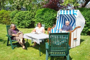A garden setting with a table and chairs, a covered chair, and a hedge in the background. - "Mullewap" at the Koch holiday farm (Schönhagen)