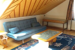 Ein Zimmer mit einem blauen Sofa, einem Holztisch und einem gemusterten Teppich.