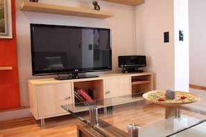 A modern living room with a flat-screen TV on a wooden cabinet, a glass coffee table with a candle, and a small black speaker. - Holiday apartment in the Harz Mountains with 2 bedrooms (Bad Harzburg)