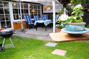 An outdoor patio area with a table and chairs, a hanging flower pot, and a barbecue grill. - Holiday apartment in the Harz Mountains with 2 bedrooms (Bad Harzburg)