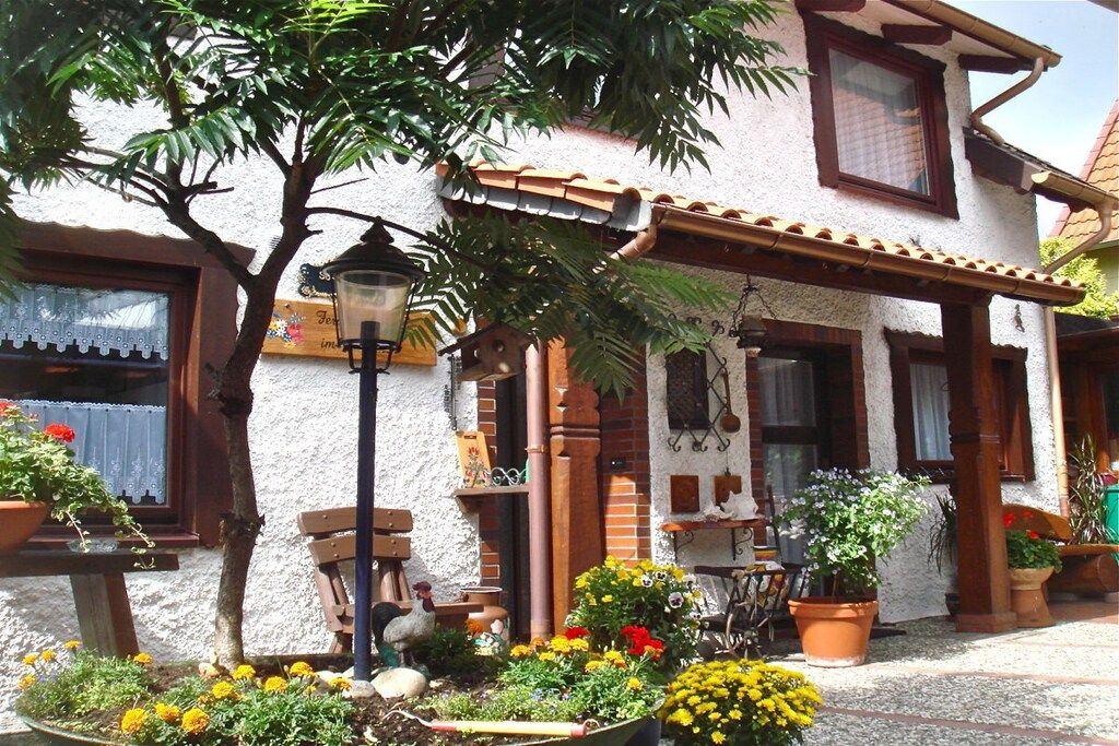 Ein traditionelles Gebäude mit einem Ziegeldach, einem Balkon mit Tisch und Stühlen sowie verschiedenen Kübelpflanzen.