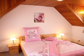 A bedroom with a sloped ceiling, a single bed with pink bedding, two bedside lamps, and a wall-mounted picture of a rose. - Holiday apartment in the Harz Mountains with 2 bedrooms (Bad Harzburg)
