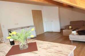 Ein Wohnzimmer mit Holzboden, einer Couch, einem Tisch mit Blumenvase und einer Tür im Hintergrund.