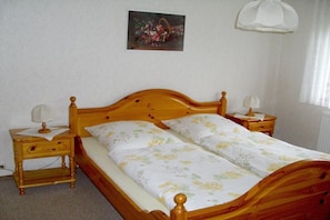 A bedroom with a wooden bed, two bedside tables, a nightstand, a wall-mounted lamp, and a floral painting. - "Sunshine" in Lenzkirch (Lenzkirch)
