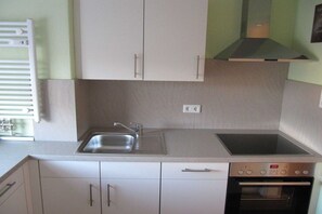 A kitchen with white cabinets, a stainless steel sink, a built-in oven, and a range hood. - Holiday apartment with 2 bedrooms (Duhnen)