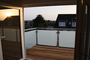 A balcony with a wooden floor and metal railing, overlooking a residential area with houses and trees. - Holiday apartment with 2 bedrooms (Duhnen)