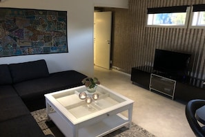 Ein modernes Wohnzimmer mit einer Eckcouch, einem Glastisch, einem Flachbildfernseher und einem großen abstrakten Gemälde an der Wand.