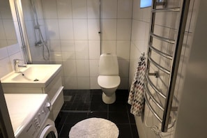 A compact bathroom with a toilet, a washing machine, a sink, and a shower enclosure. - Holiday home 25 m from Lake Nömmen (Stensjön)