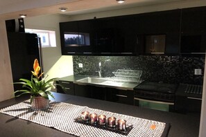 Cozinha moderna com armários escuros, pia de aço inoxidável e painel de azulejos.