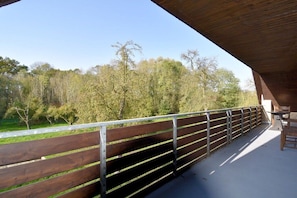 An outdoor seating area with a wooden bench and metal railing, overlooking a grassy area with trees. - Holiday home with 5 bedrooms (Wunstorf-Idensen)