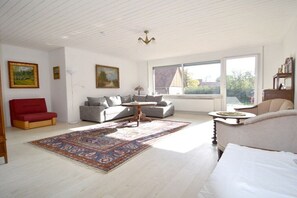 A spacious living room with a large window, a red sofa, a grey sofa, and a patterned rug. - Holiday home with 5 bedrooms (Wunstorf-Idensen)