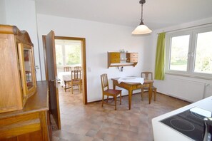 Ett rum med ett matbord, stolar, ett skåp, ett fönster med gardiner och ett element.