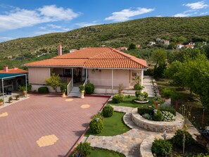 A house with a tiled roof, a covered porch, and a landscaped garden with a stone pathway. - Holiday Home 'Anastasia's Olive Grove' with Mountain View, Wi-Fi and Air Conditioning (Γούβες)