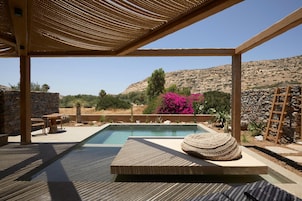Un área de piscina con un pergolado de madera, paredes de piedra y vistas a un paisaje montañoso.