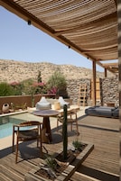 Un patio al aire libre con piscina, mobiliario y vistas a un paisaje montañoso.