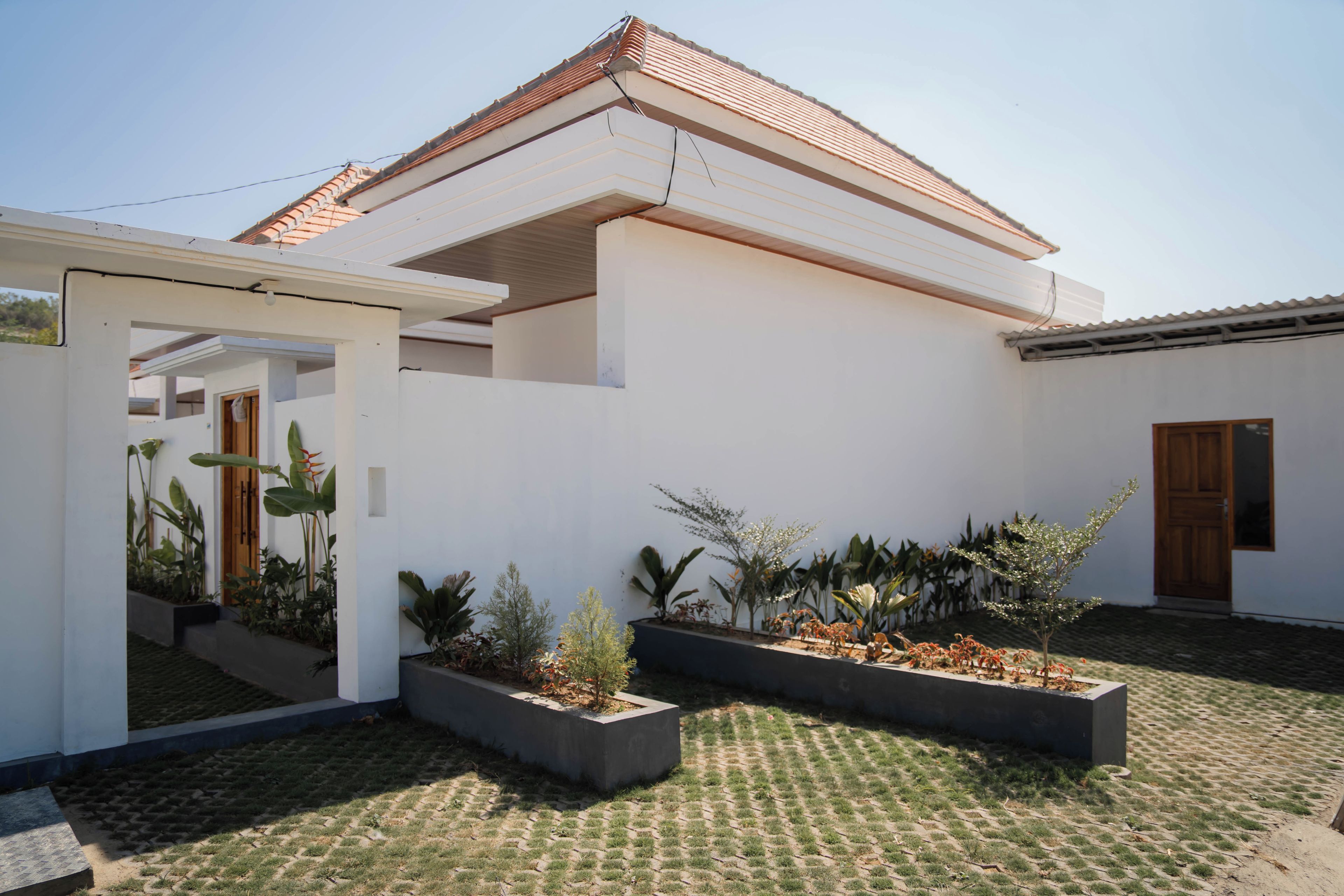A modern house with a tiled roof, a covered patio area, and a garden with various plants.