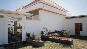 A modern house with a tiled roof, a covered patio area, and a garden with various plants.