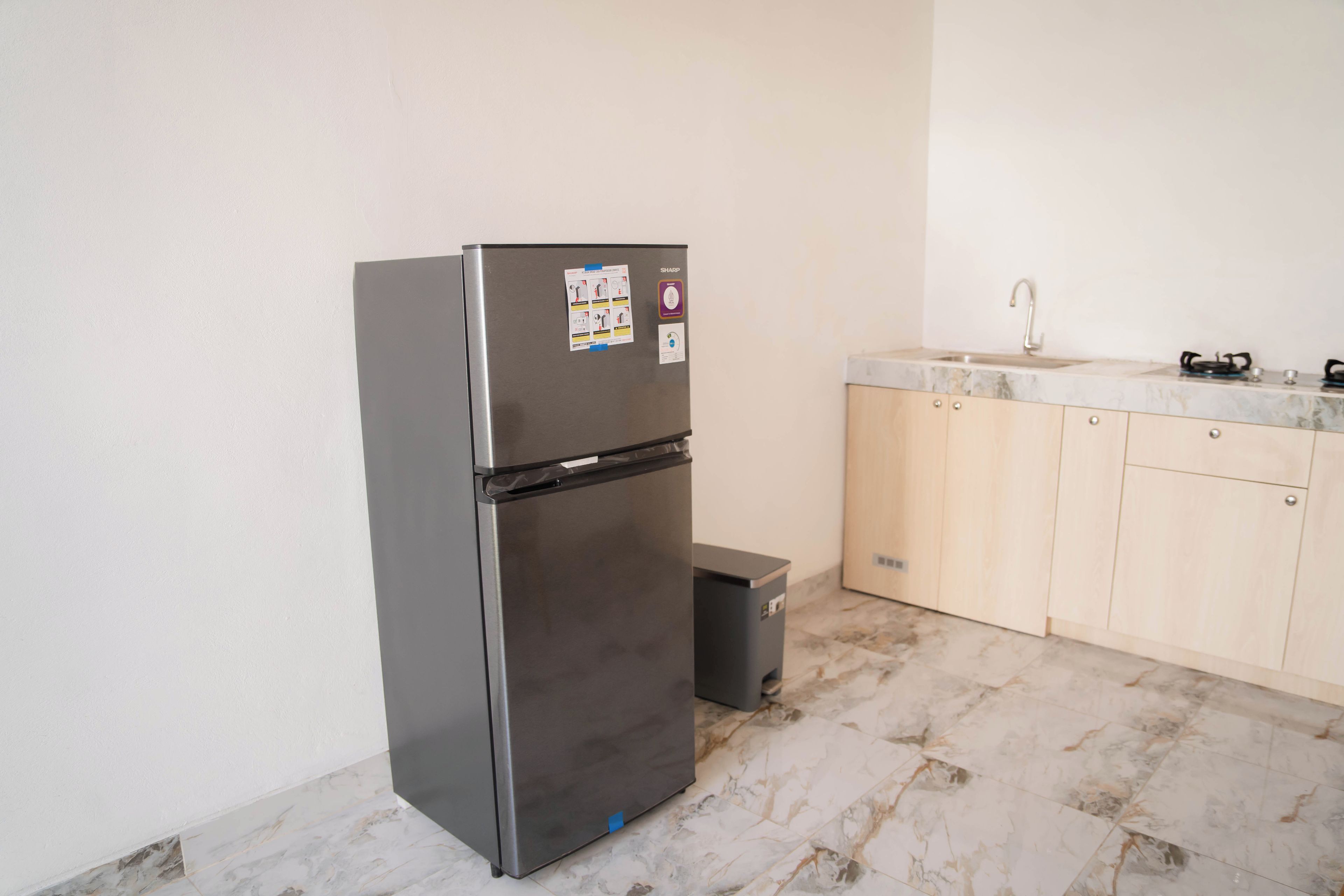 Una cocina compacta con refrigerador de acero inoxidable, un lavamanos y armarios de madera.