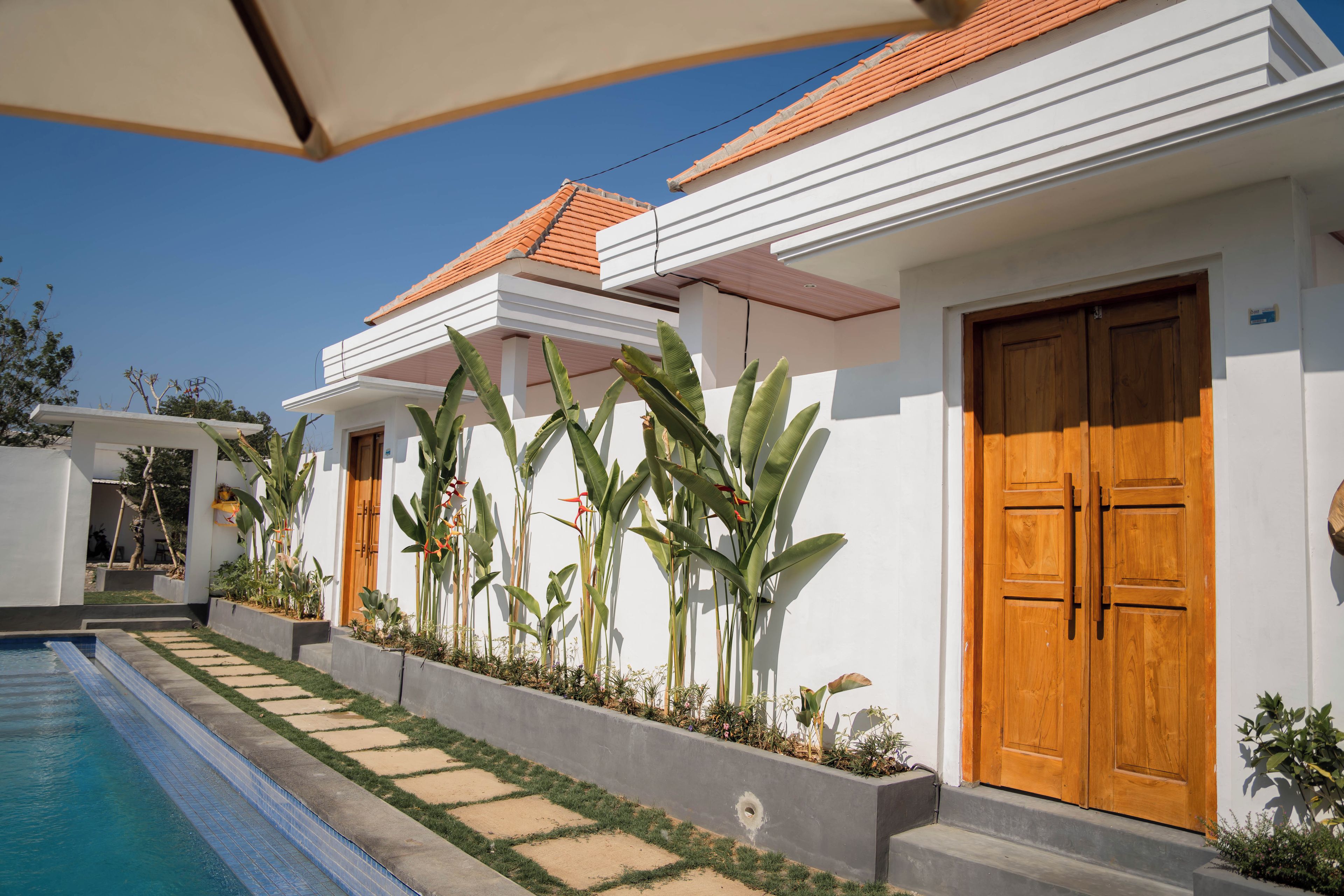 A residential building with a swimming pool, wooden doors, and tropical plants.