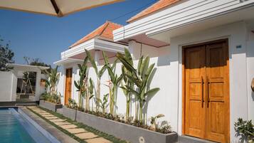 A residential building with a swimming pool, wooden doors, and tropical plants.