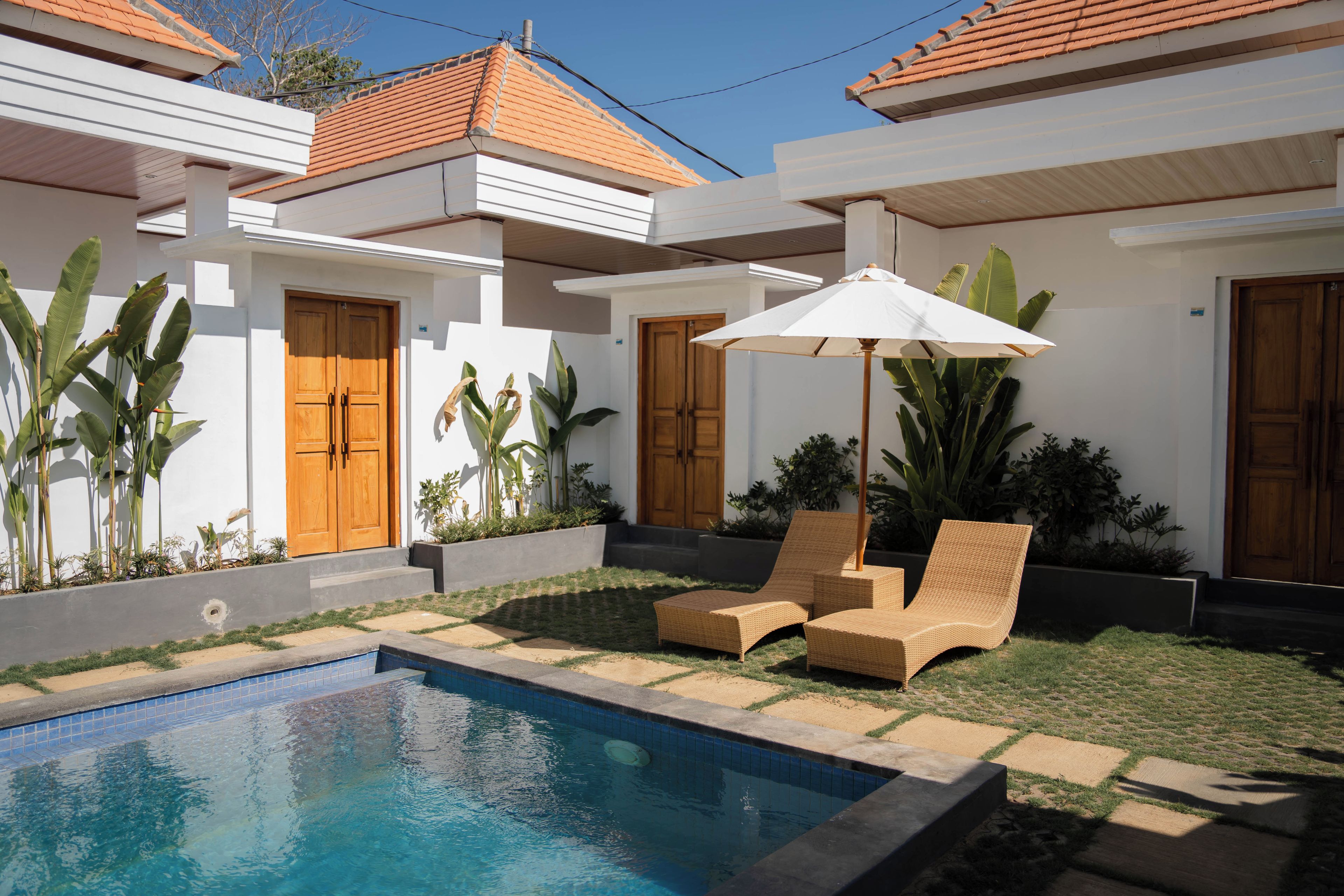 Une piscine dotée de chaises longues et d’un parasol, entourée d’un jardin où poussent différentes espèces de plantes.
