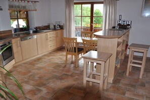 A kitchen with wooden cabinets, a stove, and a dining area with chairs and a table. - Holiday apartment with 1 bedroom (Rieden am Forggensee)