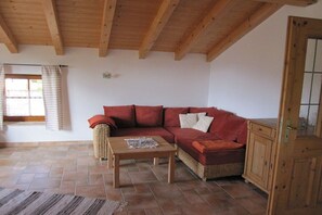 A room with a wooden ceiling, a red sofa, a wicker chair, a wooden table, and a cabinet. - Holiday apartment with 1 bedroom (Rieden am Forggensee)