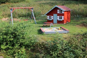 Une maisonnette en bois rouge avec une balançoire et une table de pique-nique, le tout installé dans un espace herbeux.