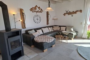 A modern living room with a sectional sofa, a fireplace, a clock, and decorative wall art. - Holiday home Harz with heart 4 (Braunlage OT Hohegeiß)
