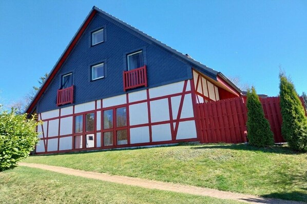 Et tosidet hus med saddeltag, en synlig fordør og et rødt hegn.