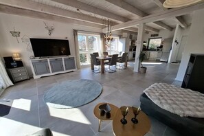 Un vaste espace de vie comprenant un grand téléviseur à écran plat, une table à manger avec des chaises, un canapé et une table basse ronde avec des verres.