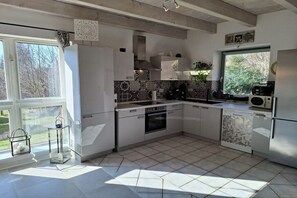 A modern kitchen with white cabinetry, a tiled backsplash, and a view of the outdoors through a large window. - Holiday home Harz with heart 4 (Braunlage OT Hohegeiß)