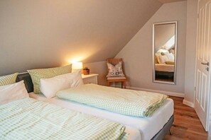 A bedroom with two beds, a nightstand, a chair, and a mirror reflecting the room. - Holiday home with 1 bedroom (Maasholm-Bad)