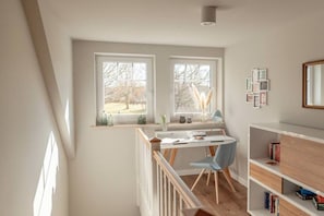 A room with a desk, chair, and bookshelf, with two windows providing a view of the outdoors. - Holiday home with 1 bedroom (Maasholm-Bad)