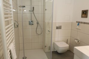 A modern bathroom with a glass shower enclosure, a toilet, and a towel rack. - Apartment 15 in Villa Meeresblau (Cuxhaven)