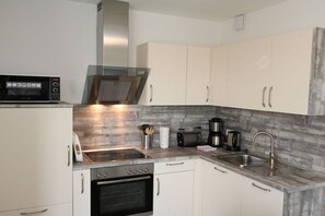 A compact kitchen with a microwave, stove, sink, and cabinets. - Apartment 15 in Villa Meeresblau (Cuxhaven)