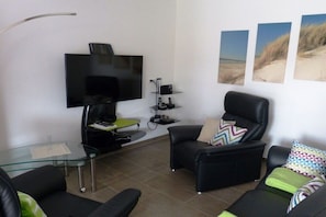 A living room with a flat-screen TV, a glass coffee table, two black sofas, and a black armchair. - Holiday home in Borkum with swimming pool (Borkum)