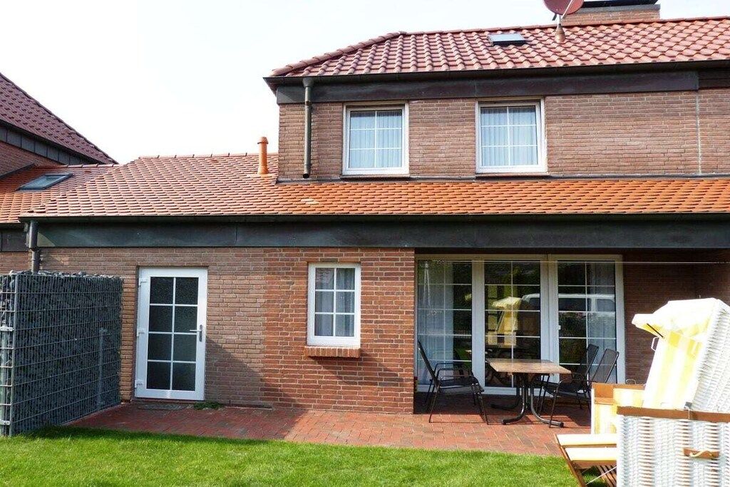 Une maison à deux étages, construite en briques, avec un toit en tuiles, une cour arrière clôturée et une terrasse aménagée avec du mobilier d’extérieur.