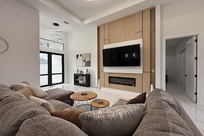 A modern living room with a large flat-screen TV, a fireplace, and a large window. - Villa in Cape Coral with swimming pool (Cape Coral)