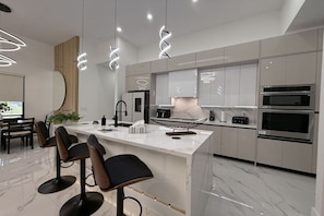 A modern kitchen with a central island, bar stools, built-in ovens, and pendant lighting. - Villa in Cape Coral with swimming pool (Cape Coral)