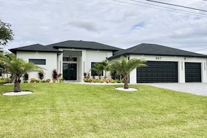 A modern two-story house with a garage, numbered 807, surrounded by a well-maintained lawn and palm trees. - Villa in Cape Coral with swimming pool (Cape Coral)