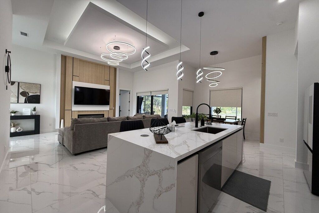 A modern kitchen with a marble island, pendant lighting, and a built-in TV.