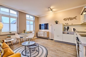 Eine moderne Küche mit Flachbildfernseher, weißen Schränken und einem Essbereich mit rundem Tisch und Stühlen.